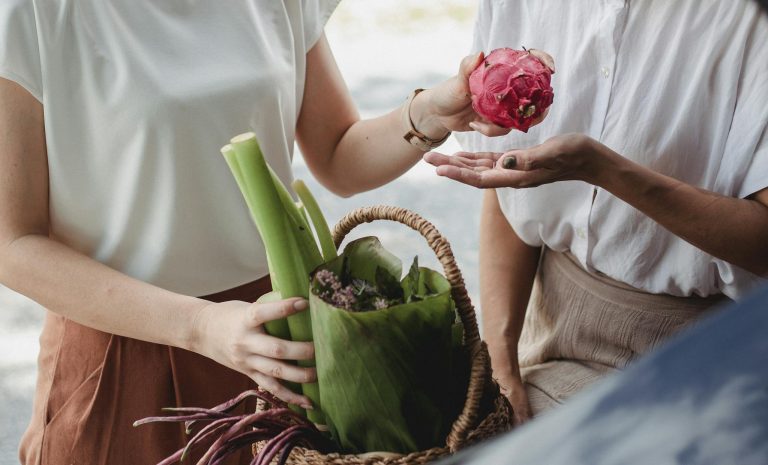 Food Security in Bangladesh, Crop unrecognizable female with basket full of green vegetables and herbs passing ripe pitaya to partner